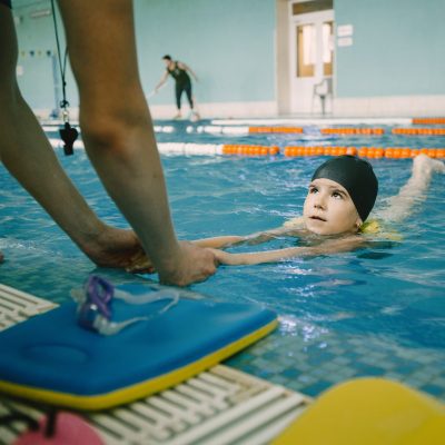 Coach teaching kid in indoor swimming pool how to swim and dive. Swimming lesson, kids development.