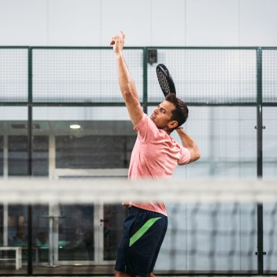 Man playing padel in a green grass padel court indoor behind the net