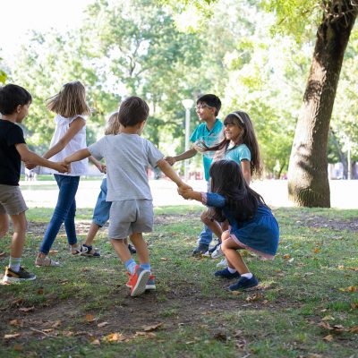Happy children playing together outdoors, dancing around on grass, enjoying outdoor activities and having fun in park. Kids party or friendship concept